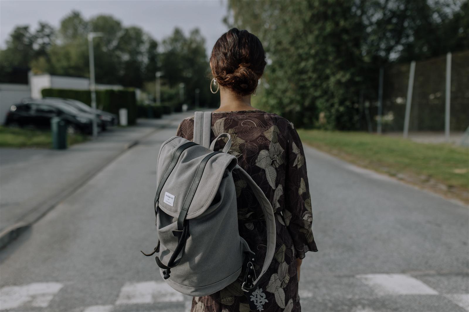 Flicka står med ryggsäck på en gata och är fotad bakifrån.